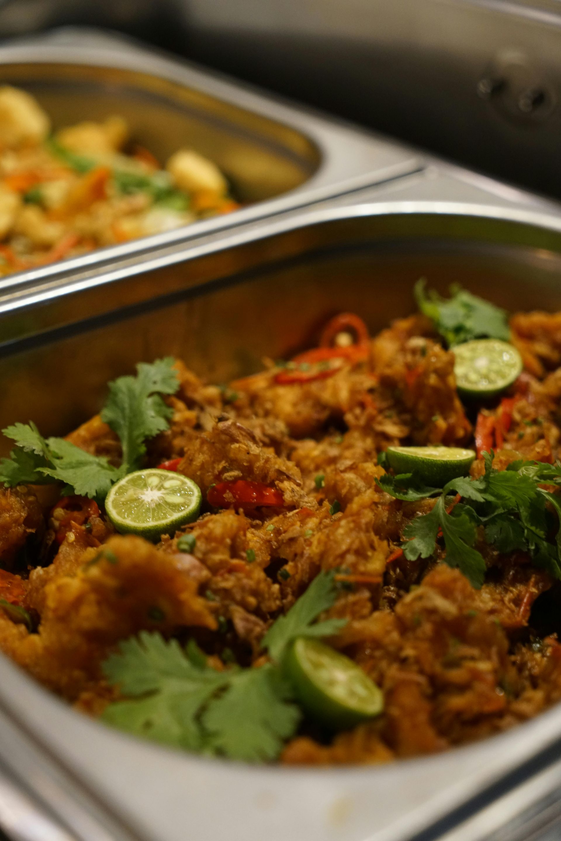 Tray of spiced curry garnished with cilantro and lime slices in a buffet line