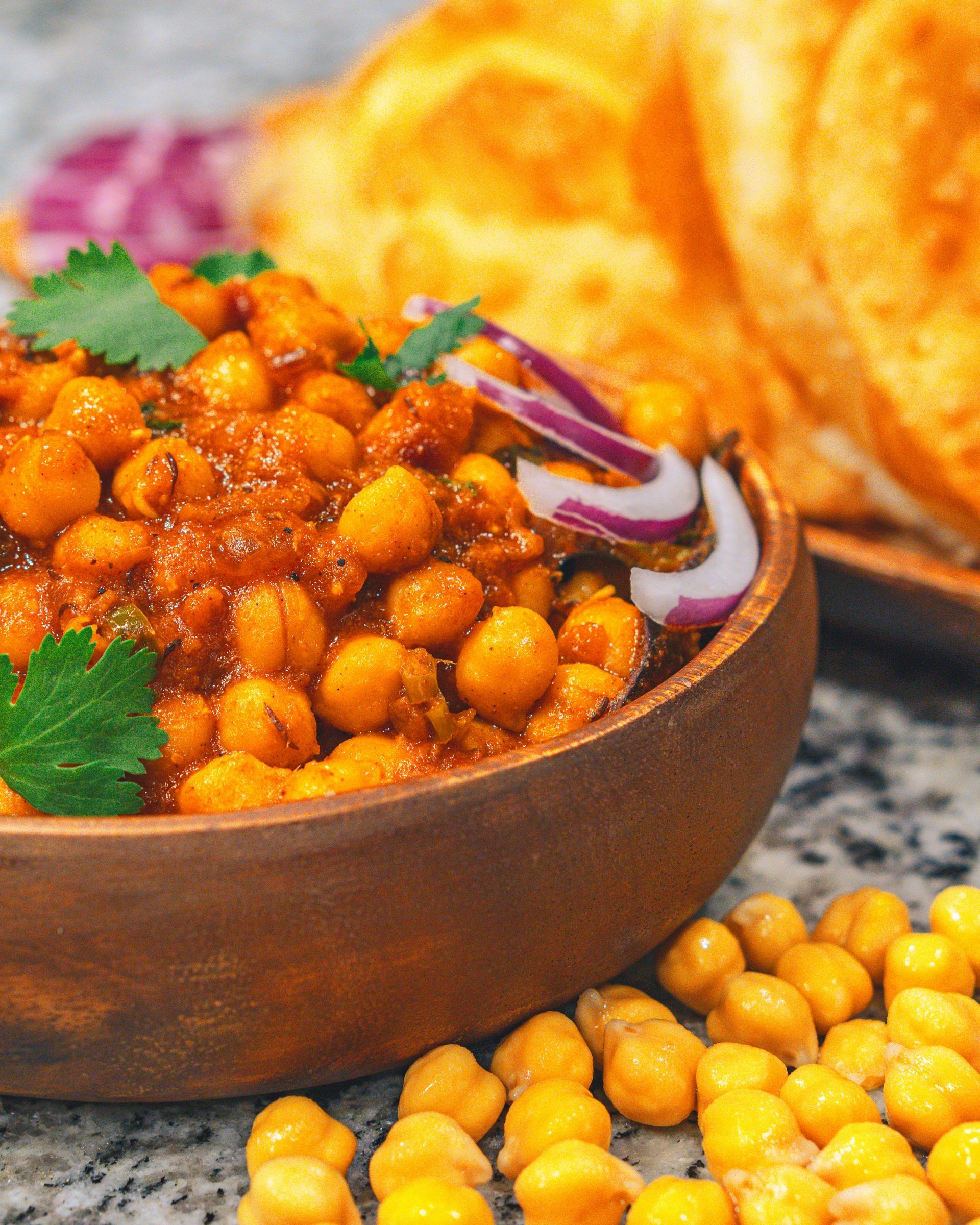 Bowl of spiced chickpeas with cilantro and red onion, beside golden fried bread on a countertop