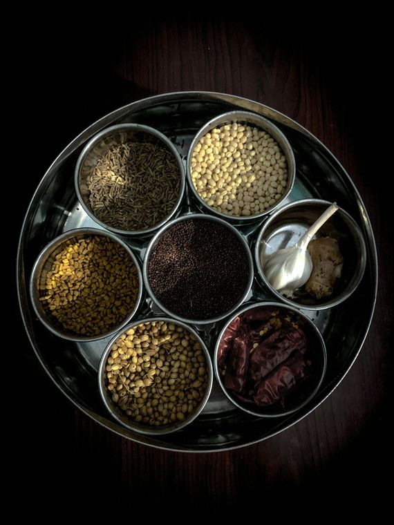 Spice tray with six compartments of assorted spices and a small spoon on a dark table
