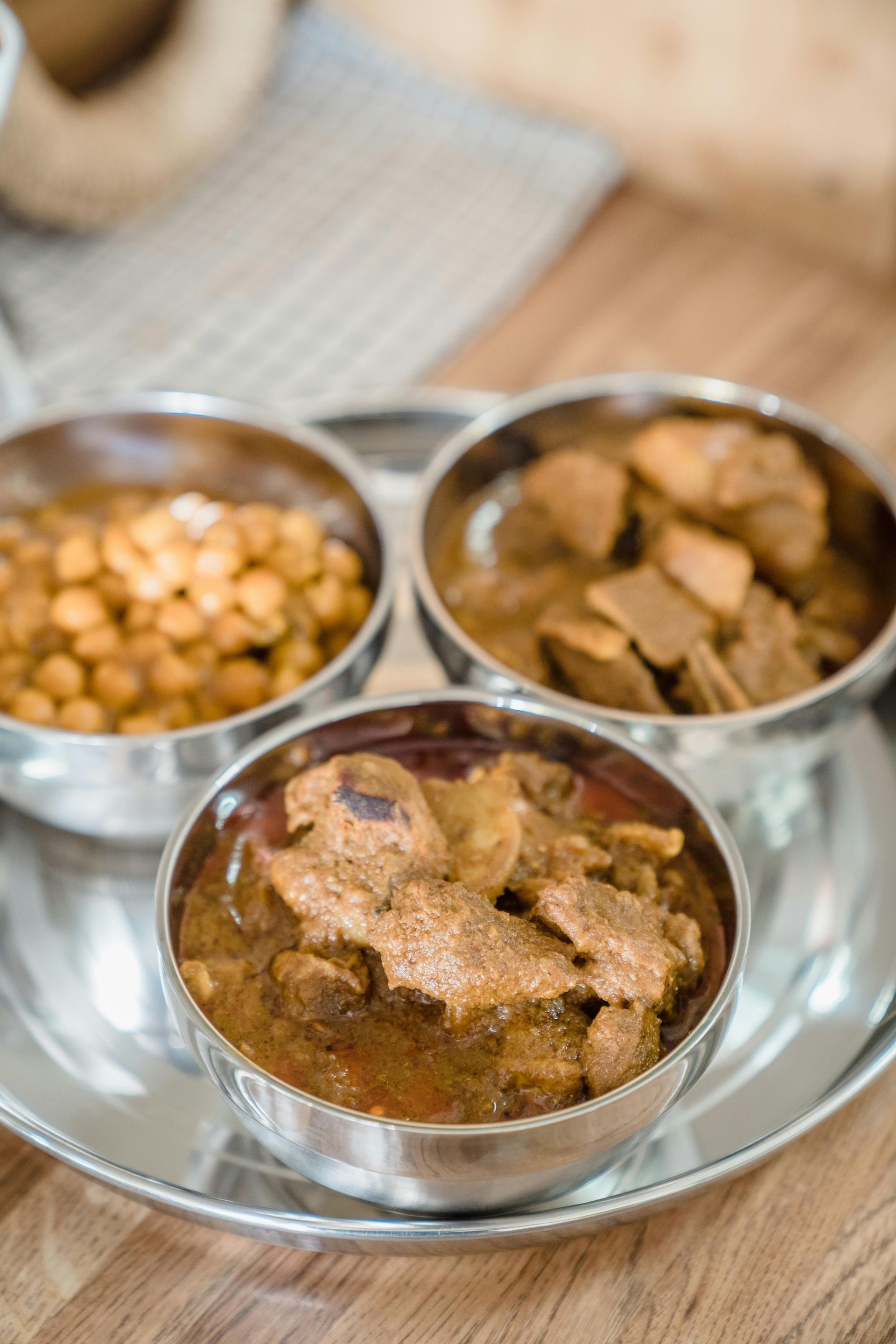 Three stainless steel bowls of Indian curry served on a tray on a wooden table