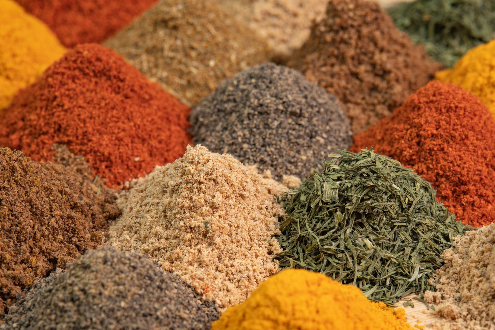 Assorted colorful ground spices and dried herbs arranged in small piles on a textured surface