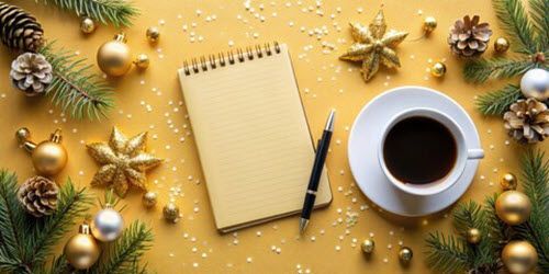 Notebook, pen, and coffee cup surrounded by Christmas ornaments and pine branches on yellow surface.
