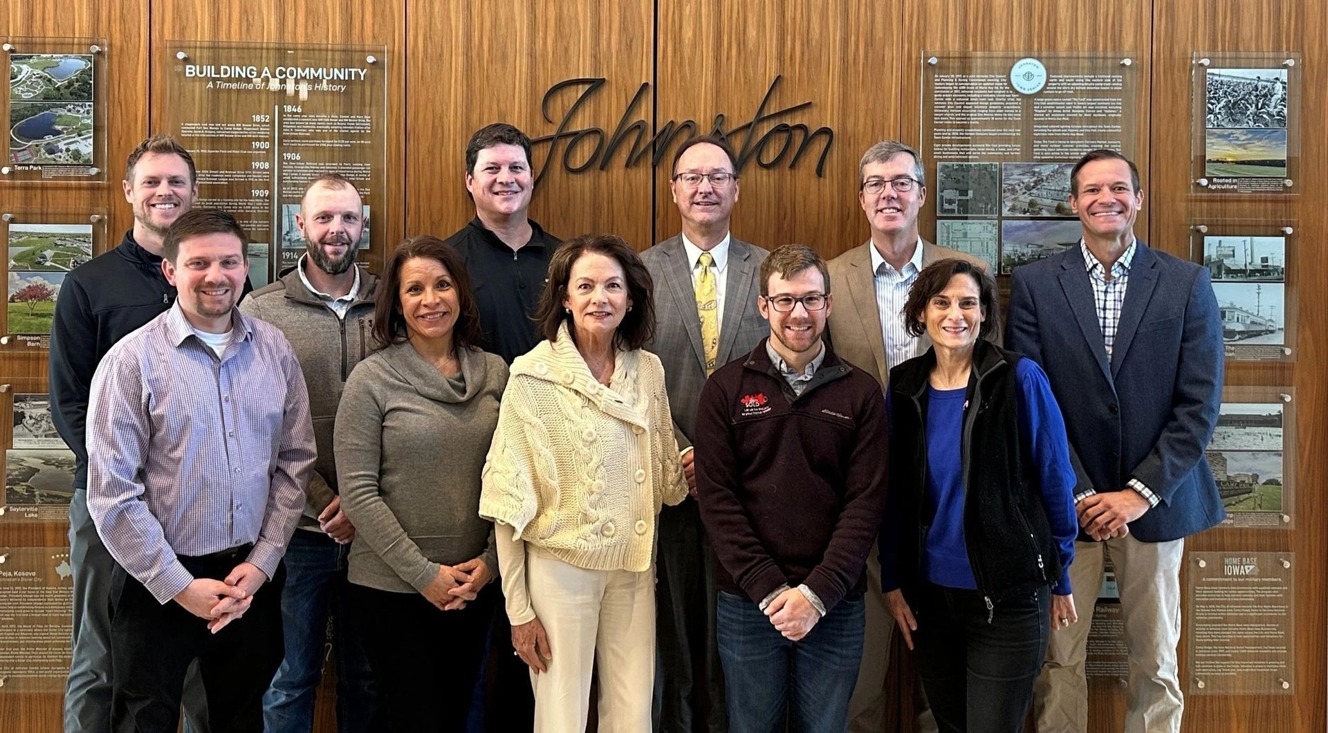 Group of people posing in front of a wood panel with "Johnston" logo.