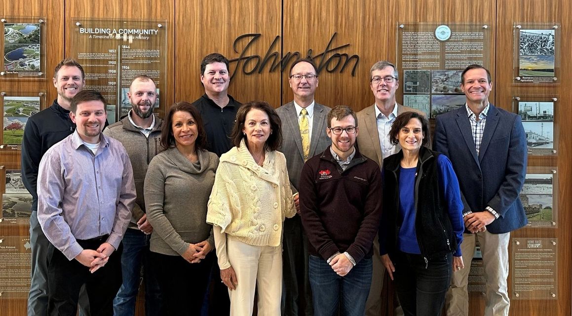 Group of people posing in front of a wood panel with "Johnston" logo.