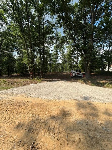 Dirt and gravel path leading into a wooded area, with a small excavator visible.