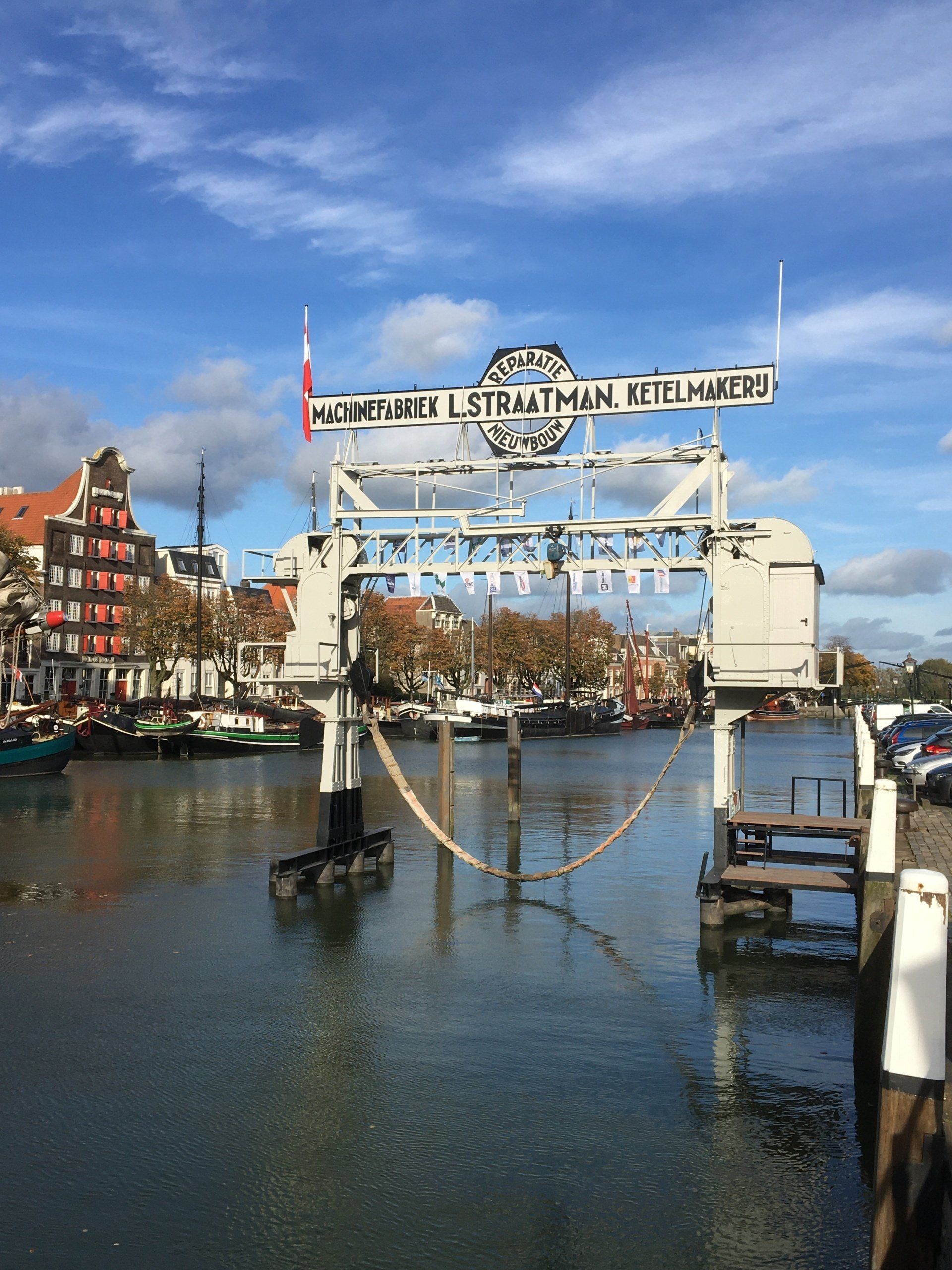 Een kanaal met een witte ophaalbrug, gebouwen en boten op de achtergrond onder een blauwe hemel.