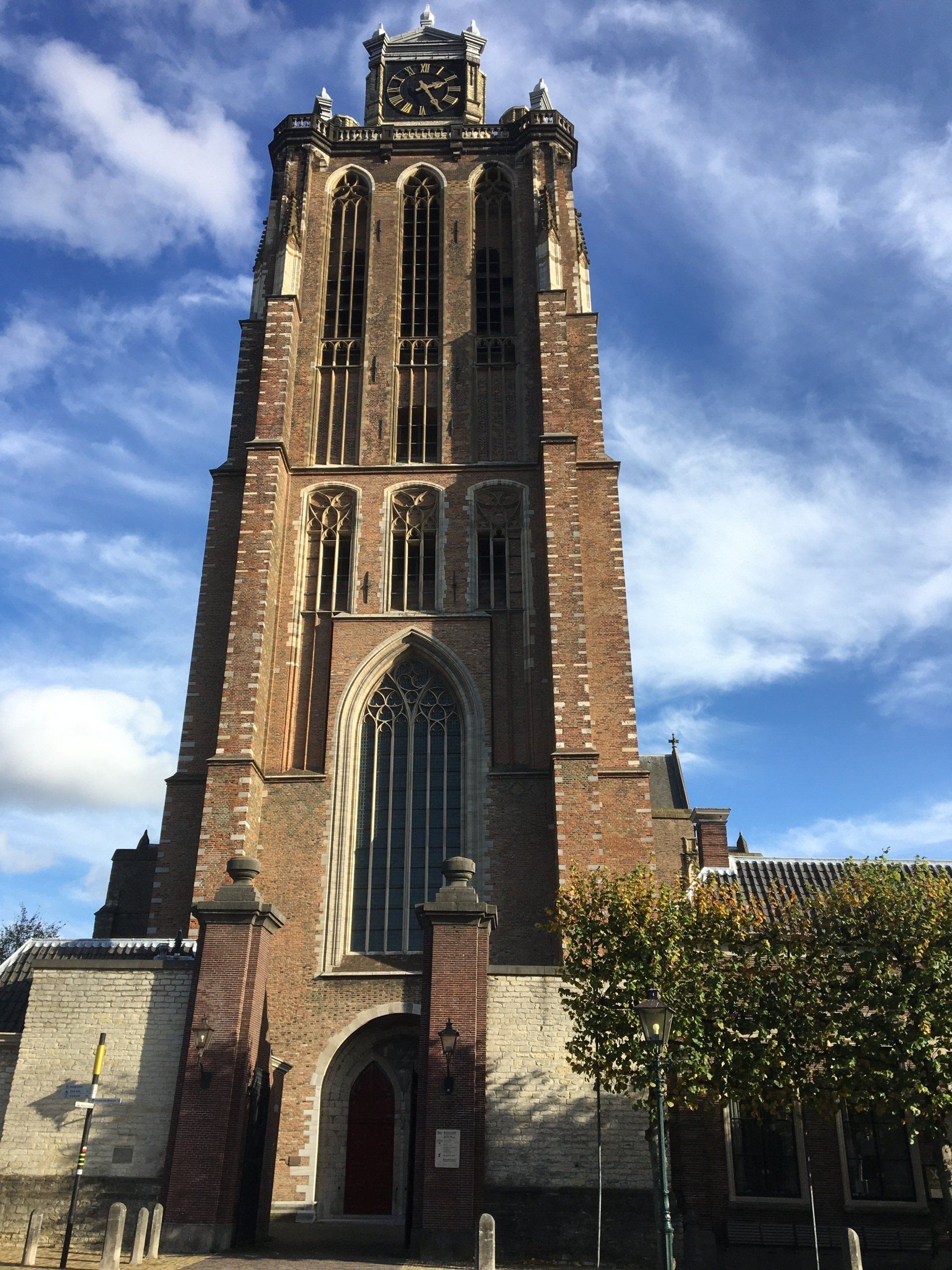 Een hoge bakstenen kerktoren tegen een blauwe hemel met wolken.