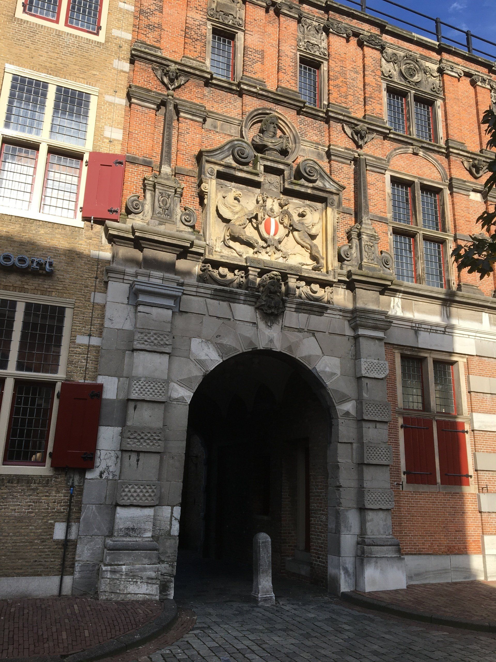 Een boogvormige ingang naar een bakstenen gebouw, bekroond met een embleem. 
