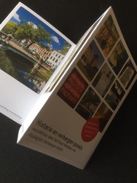 Open boekje met Nederlandse tekst en foto's van historische gebouwen, op een donkere ondergrond.