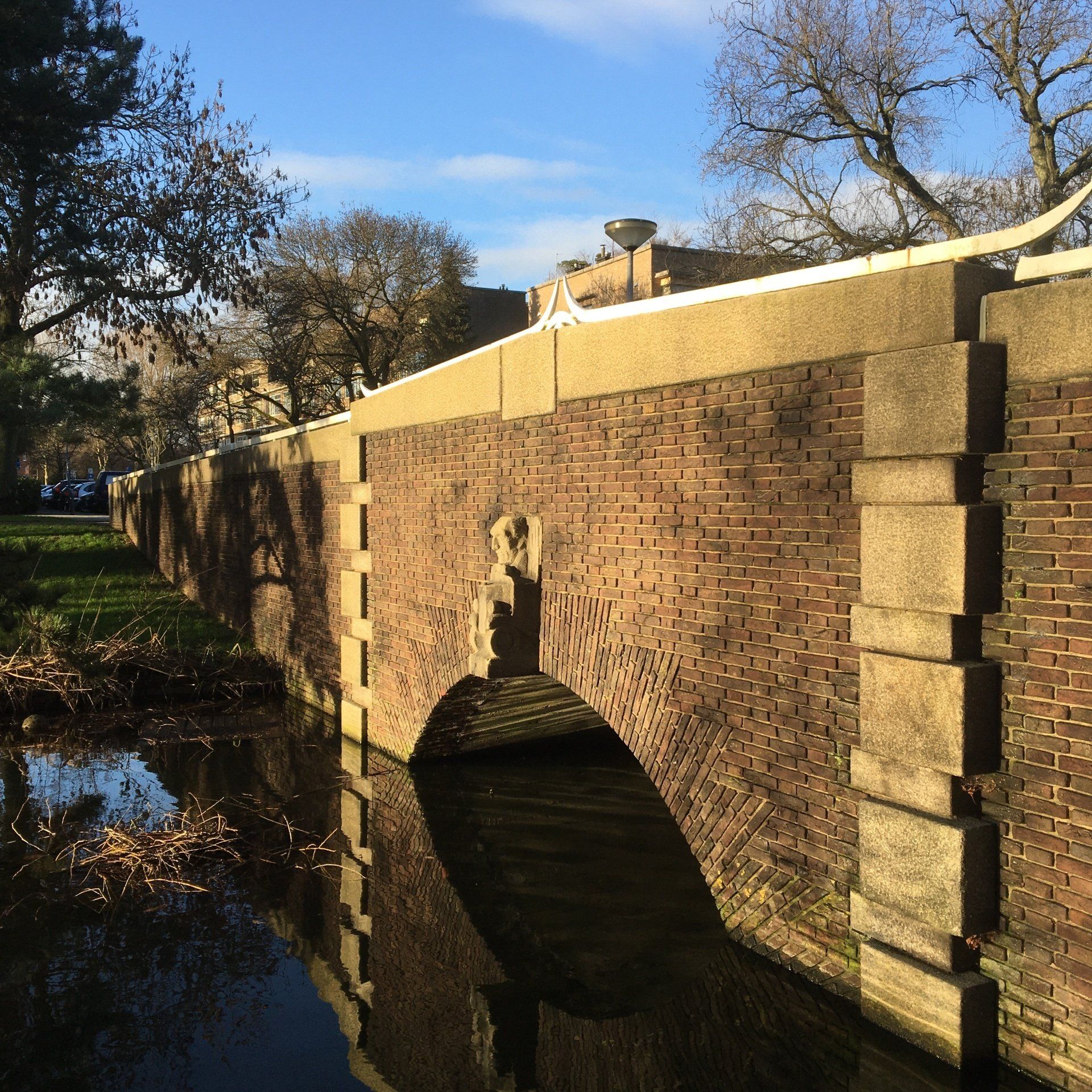 Bakstenen brug met boogvormige opening over een kanaal, bomen op de achtergrond, zonnige dag.