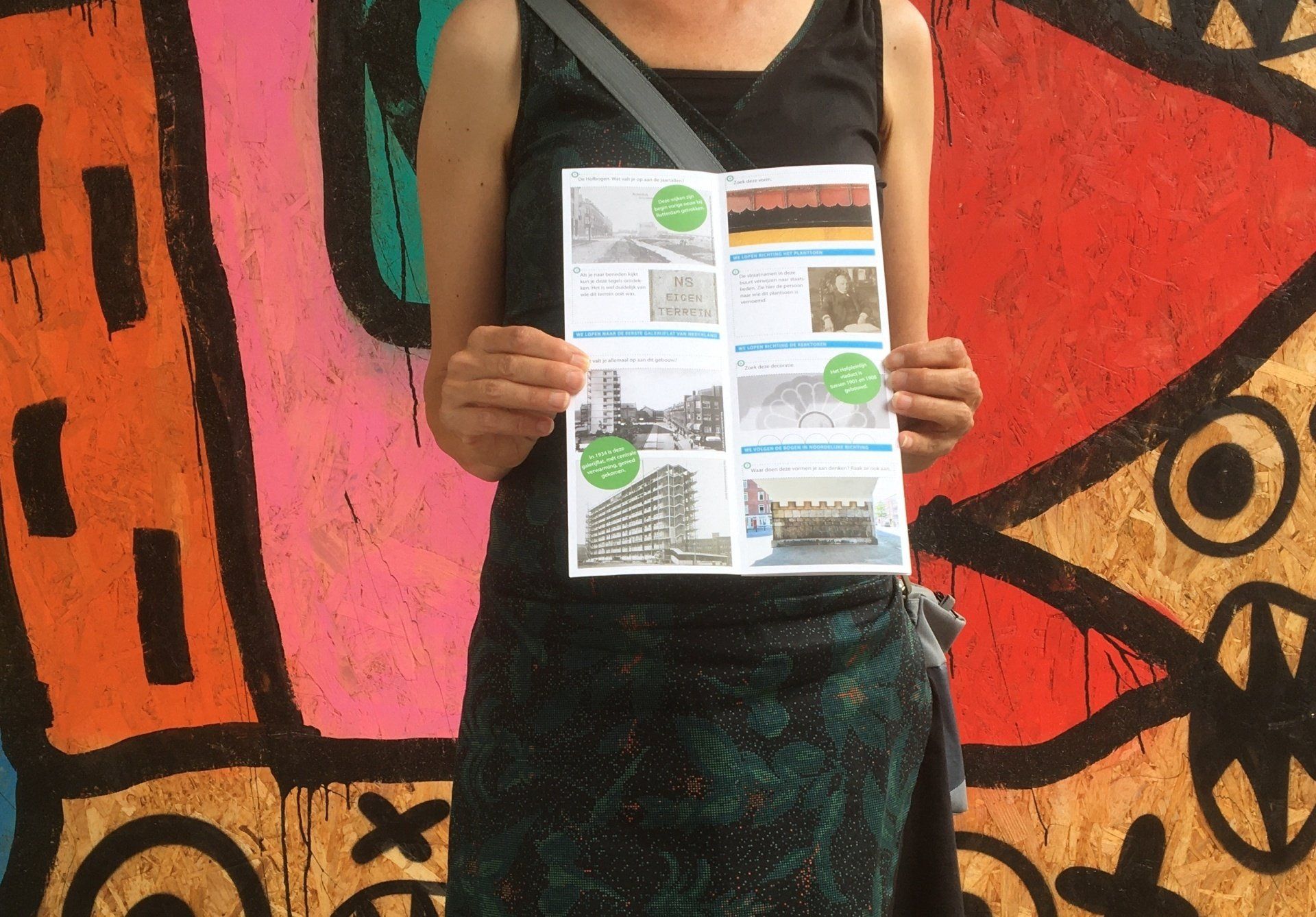Een persoon met een pamflet in zijn hand staat voor een kleurrijke graffitimuur.