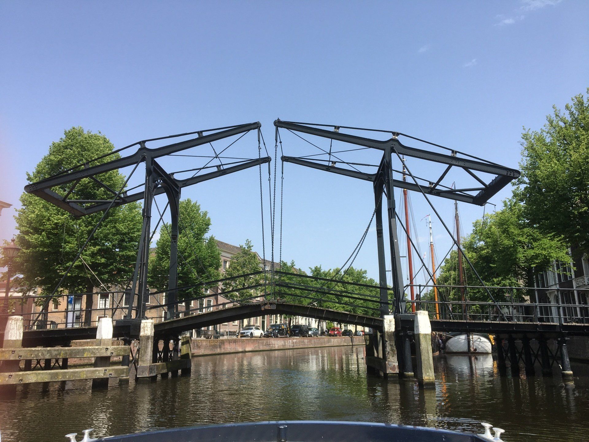 Een zwarte ophaalbrug over een kanaal in Schiedam, die omhoog staat tegen een helderblauwe hemel.