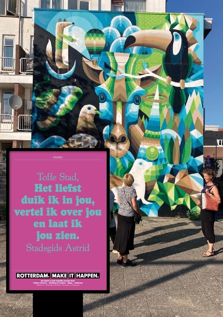 Muurschildering met abstracte vormen en tekst. Twee mensen staan ​​bij een ingelijst bord met Nederlandse tekst.