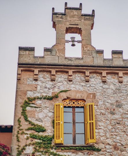 Un edificio de piedra con un campanario y una ventana con contraventanas amarillas.