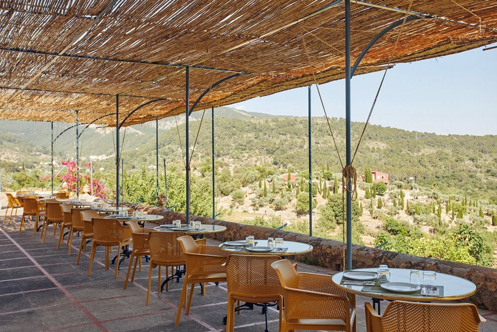 Un restaurante con mesas y sillas bajo un dosel con vista a las montañas.