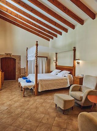Una habitación de hotel con una cama con dosel, una silla, una otomana y una cómoda.