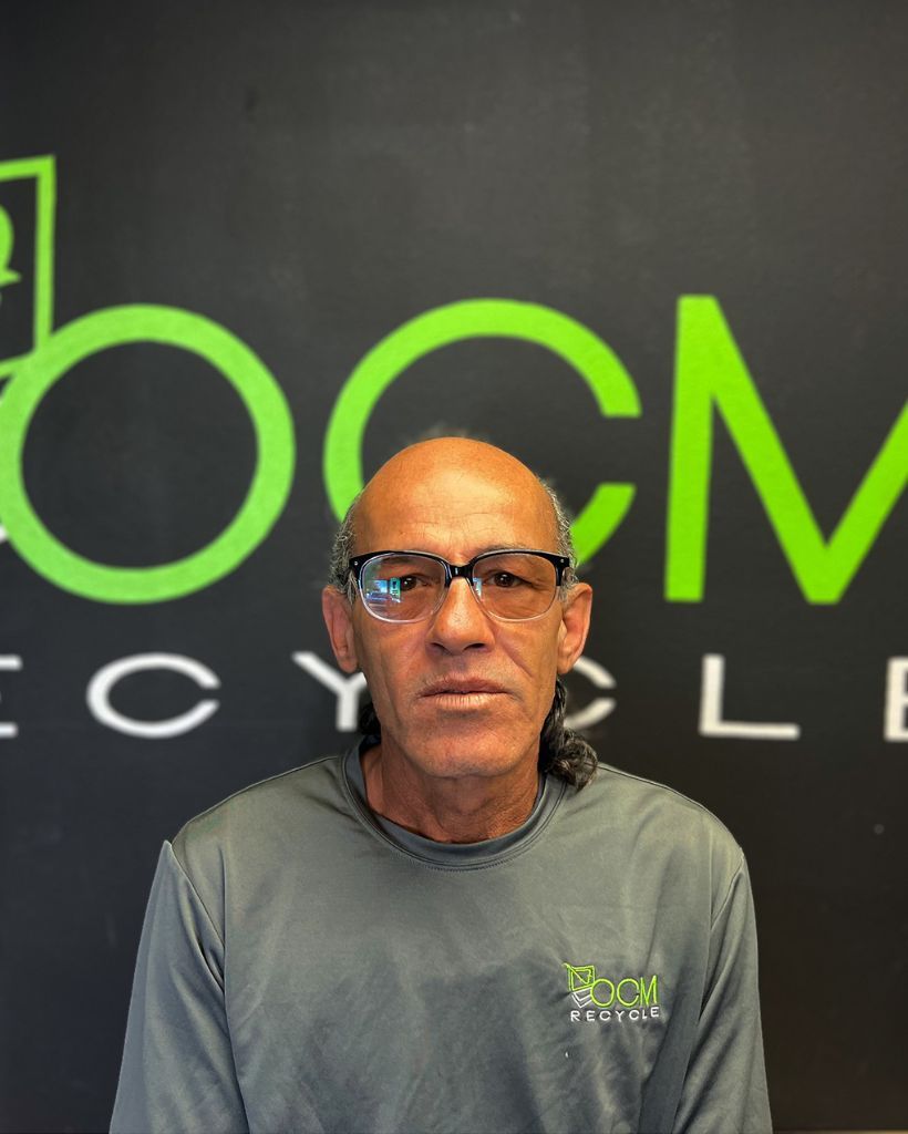 A man wearing glasses is standing in front of a sign that says ocm cycle