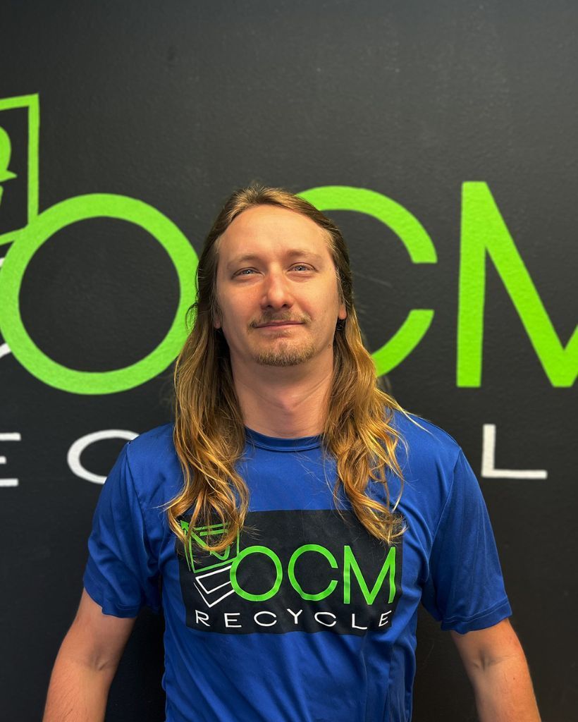 A man with long hair is wearing a blue shirt that says ocm recycling