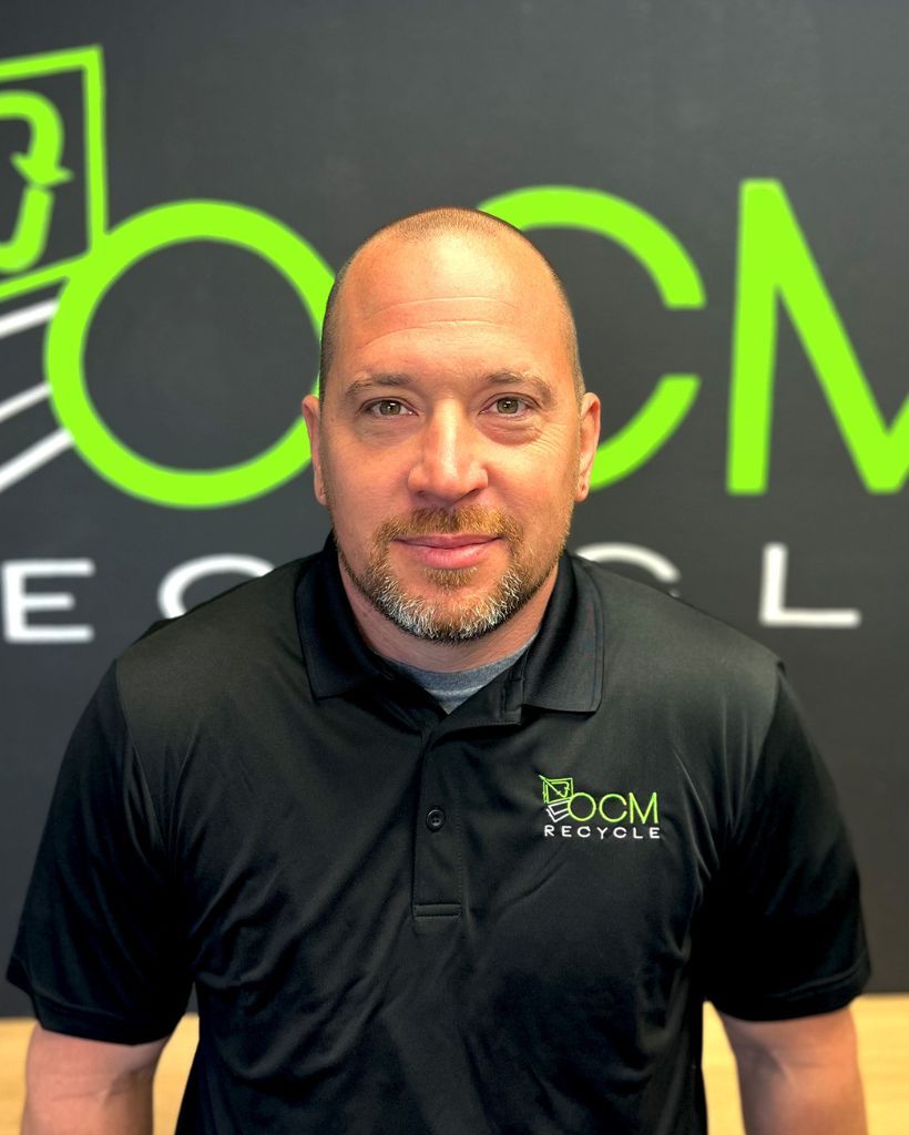 A man wearing a black polo shirt is standing in front of a large green sign.