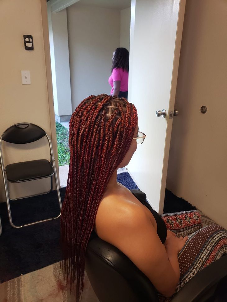 Woman with red braided hair sitting in a chair, looking toward a doorway where a child stands in a pink top.