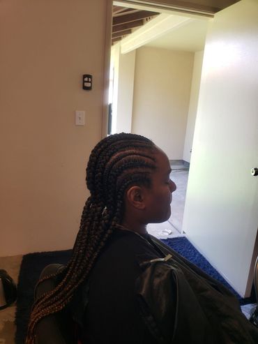 Person with braided hair seated indoors near a doorway, viewed in profile.