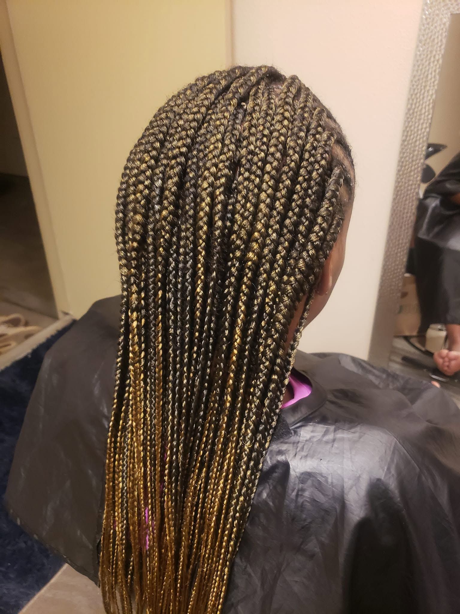 Long braided hairstyle with blonde highlights, viewed from the back in a salon chair.