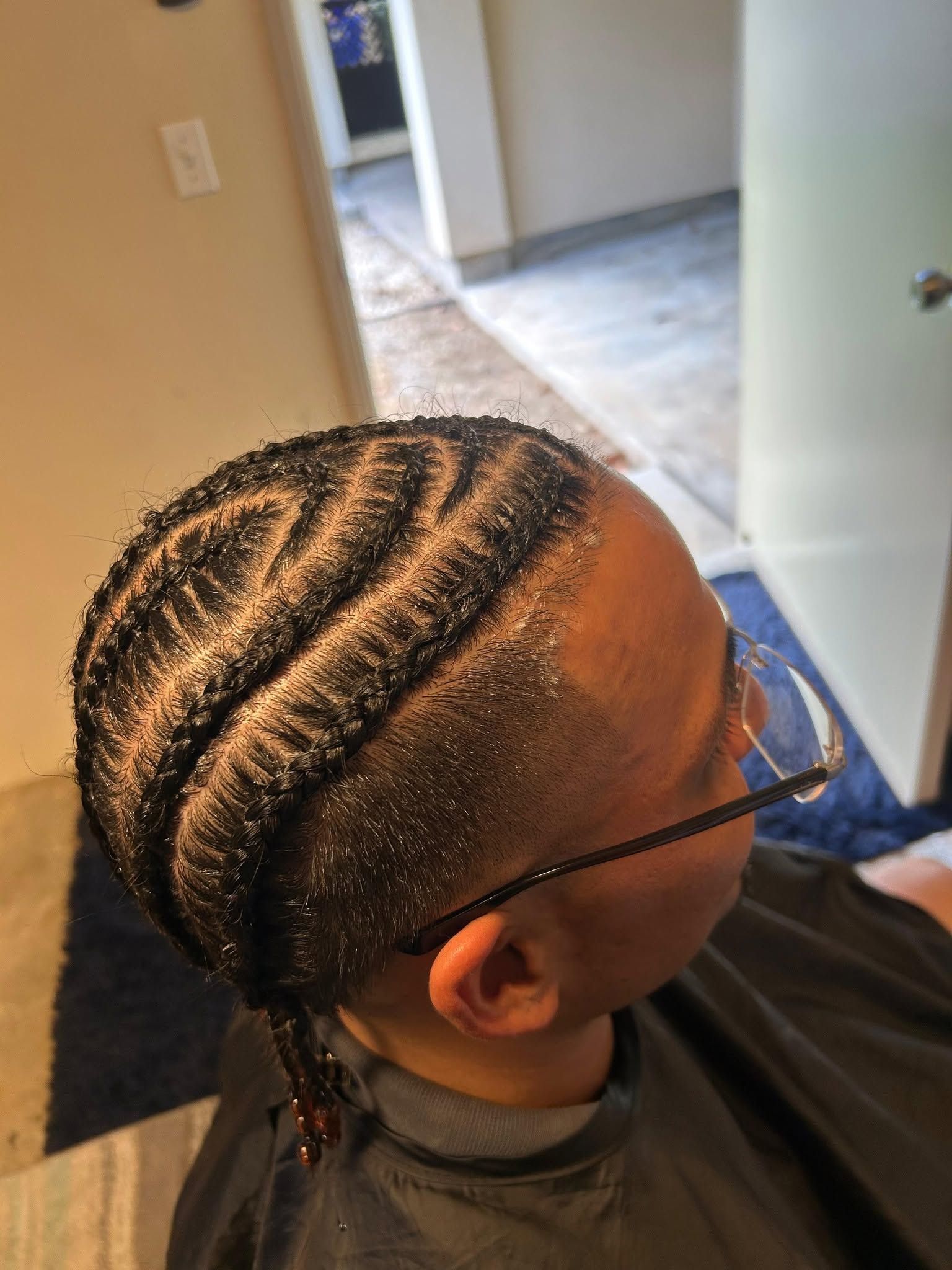 Braided hairstyle with neat cornrows and a low ponytail, viewed from the side indoors.