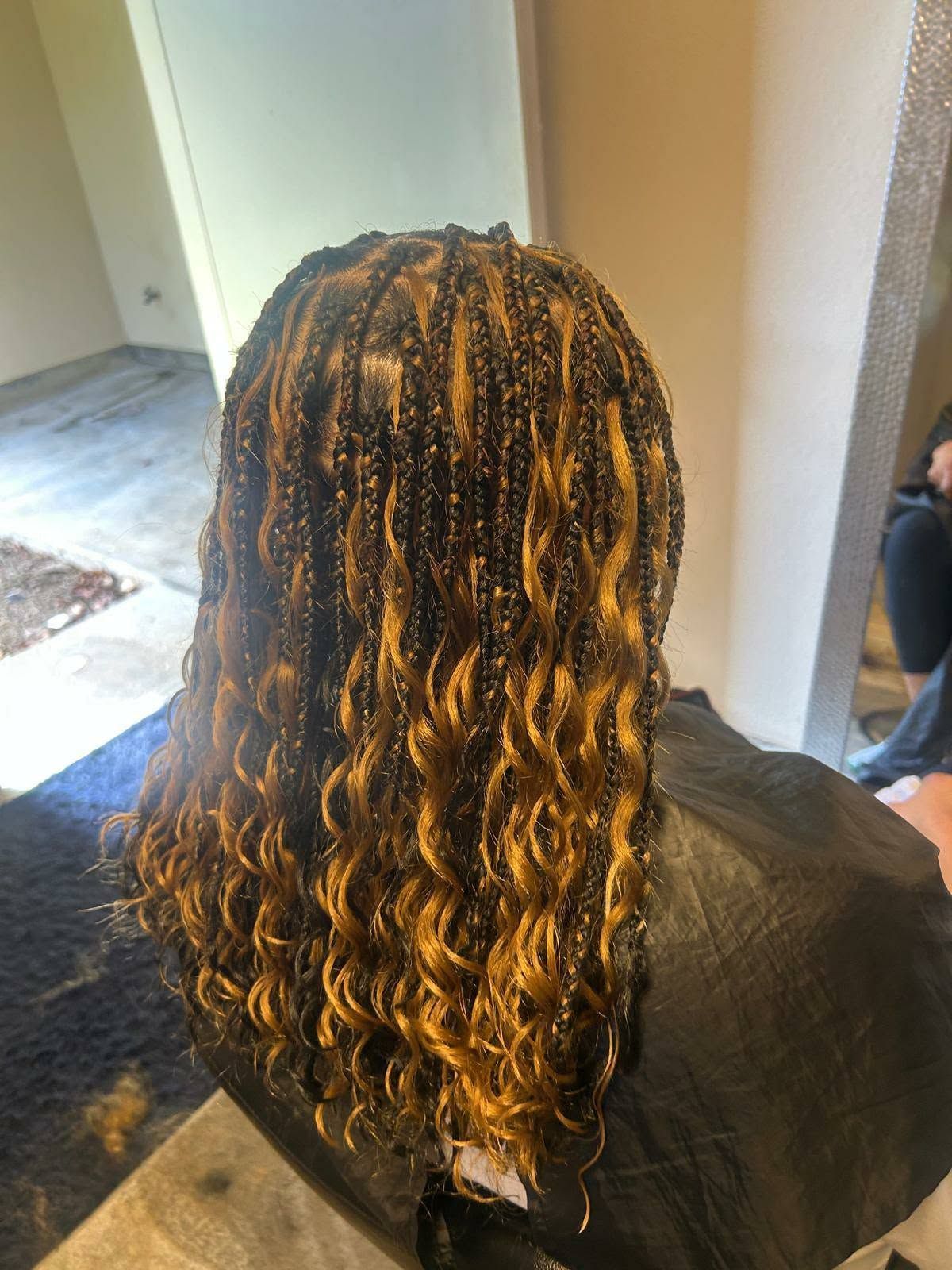 Long wavy hair with blonde highlights draped over a black salon cape, viewed from behind