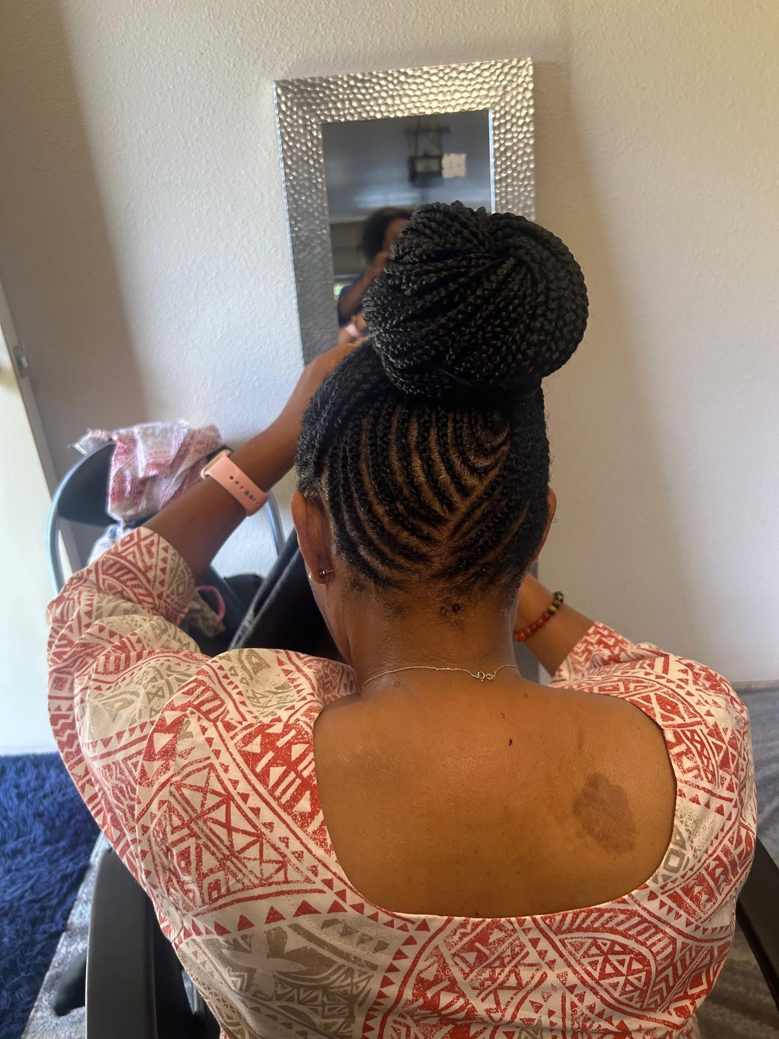 Person braiding hair in front of a mirror, wearing a patterned top.