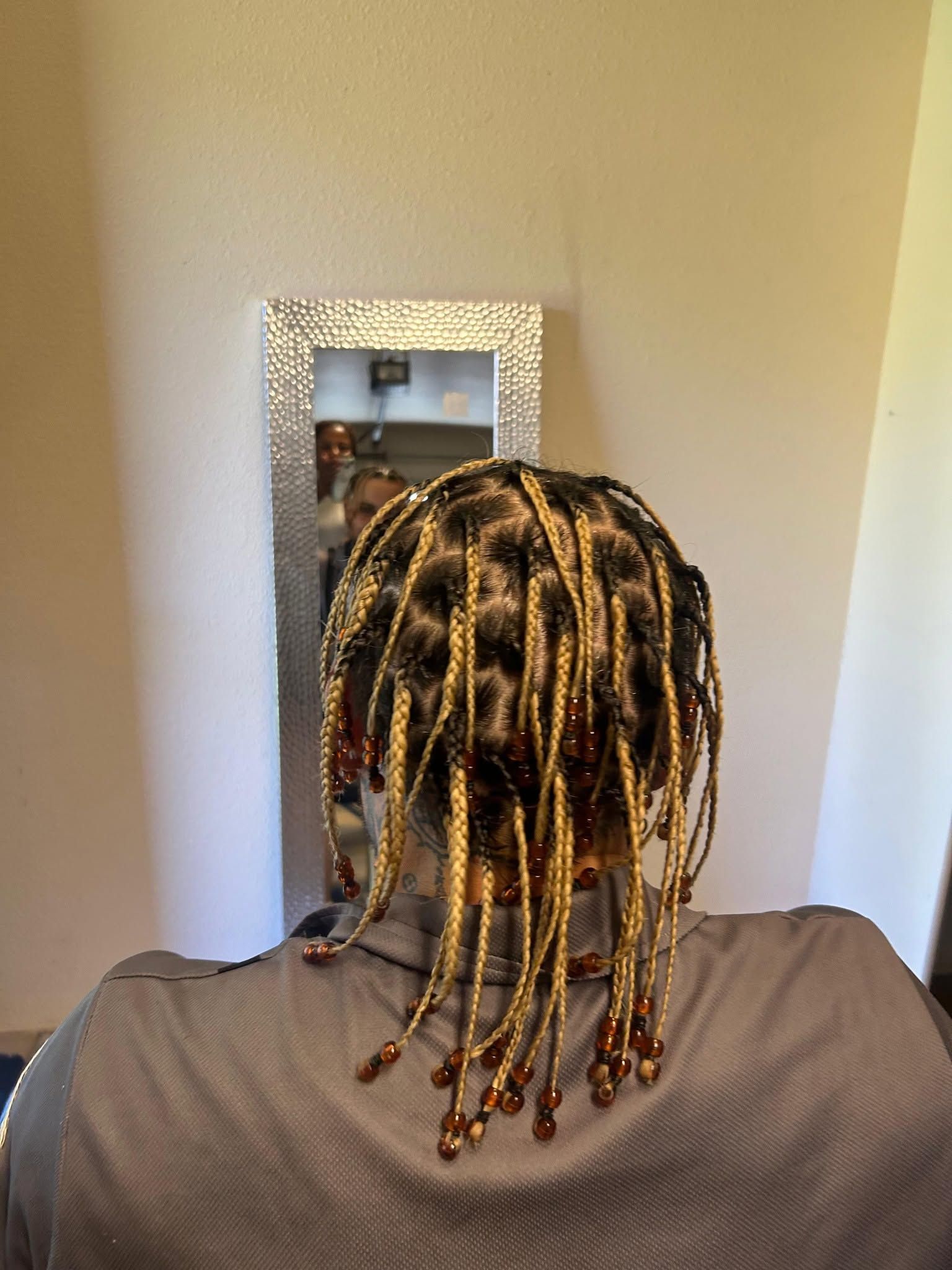 Back of a person with braided hair facing a wall mirror in a narrow hallway