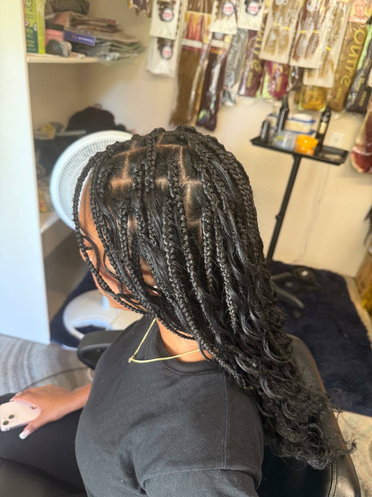 Braided hairstyle in a salon chair, side view with glossy black twists and shelves of hair products behind.