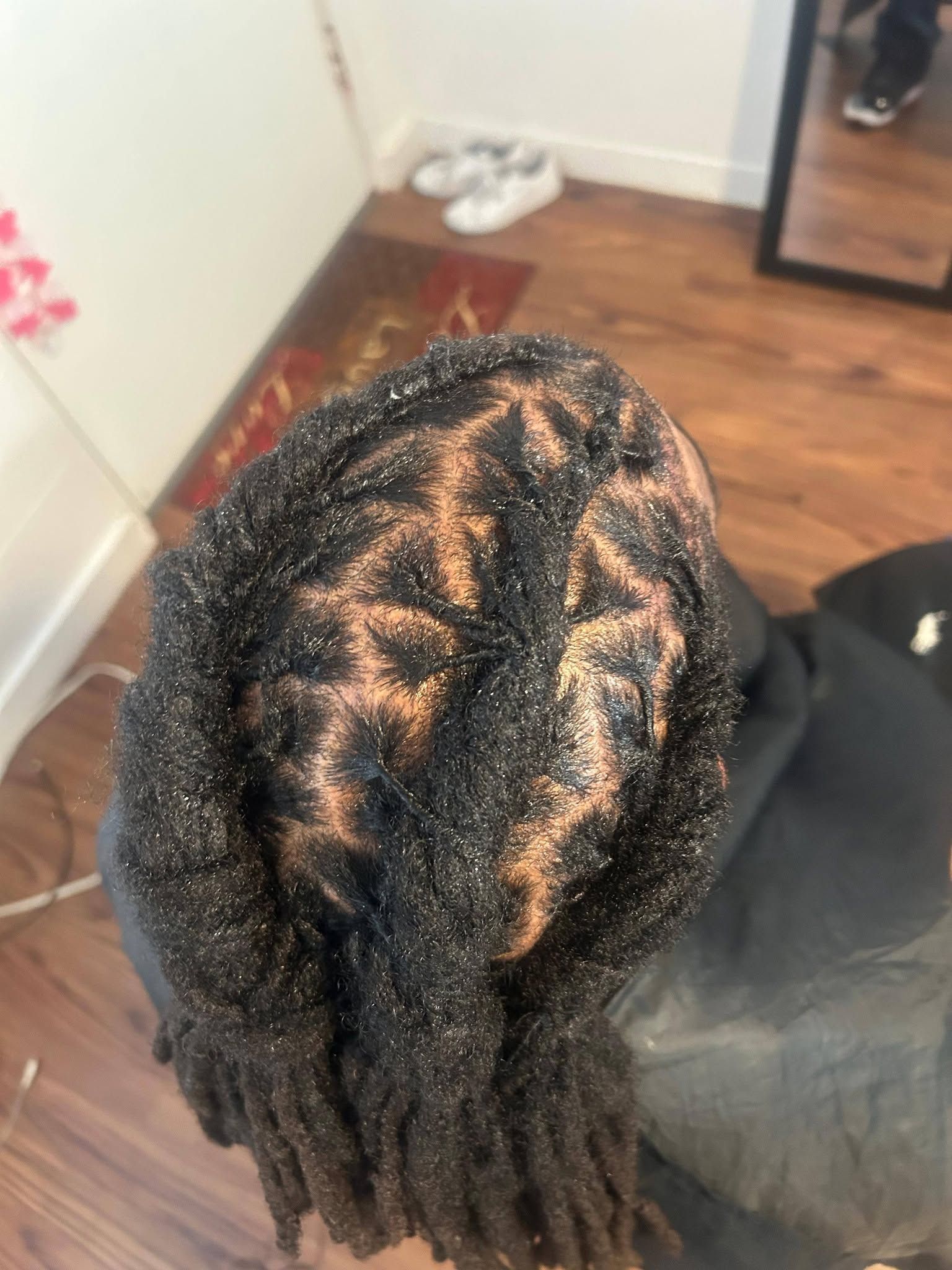 Braided hair close-up with neat parting and exposed scalp, viewed from above in a room with wooden floor.