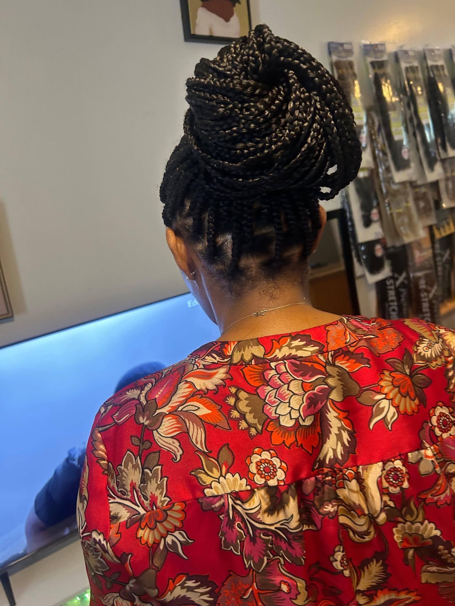 Person with braided bun facing a TV, wearing a red floral top in a room.
