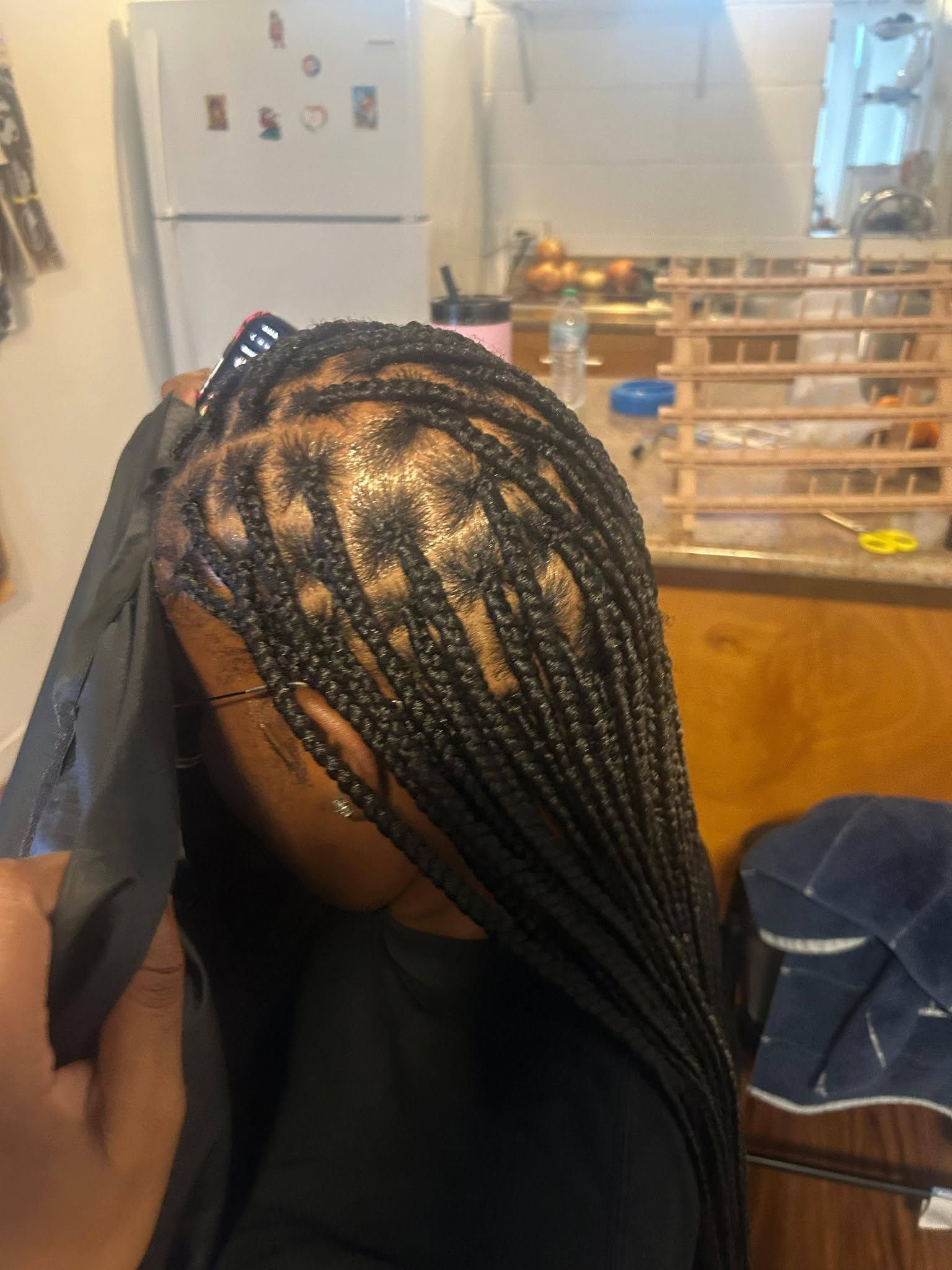 Braided hair with black and gold beads in a kitchen, head bowed over a dining table