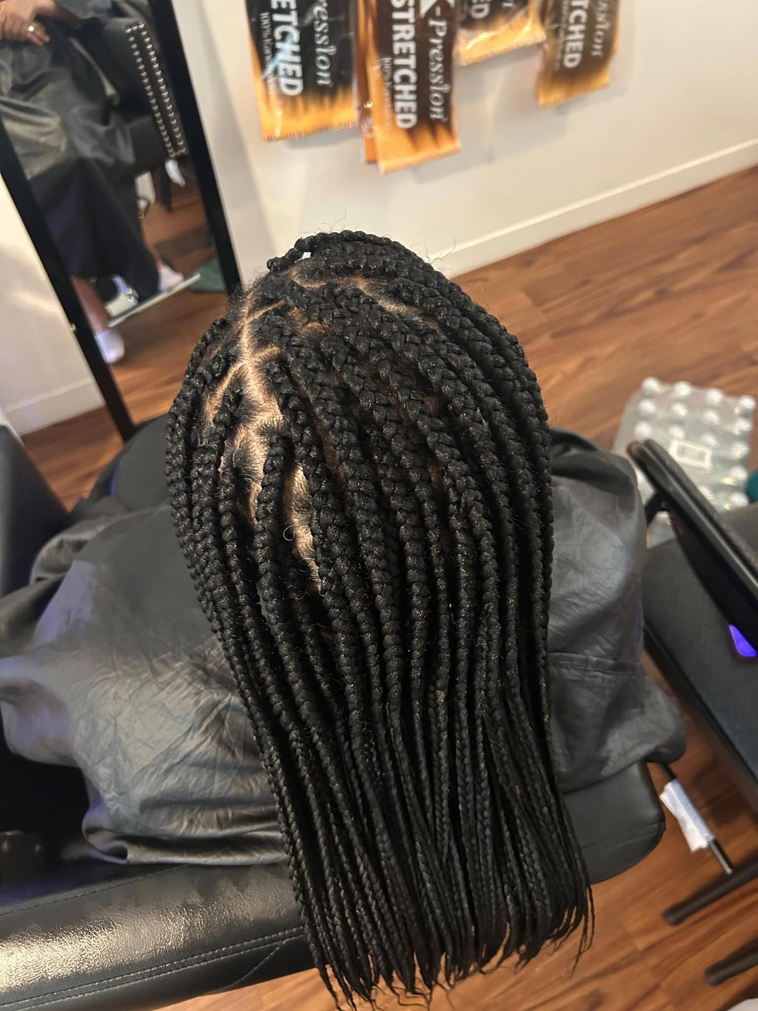 Close-up of long black braided hair on a salon chair, with hair tools nearby.