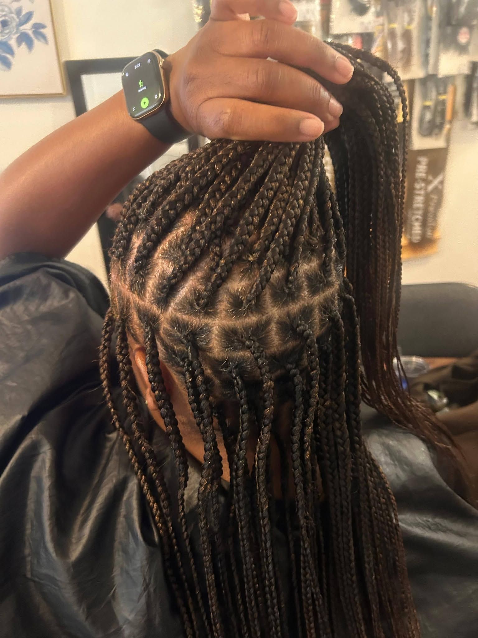 Hairdresser parting braided hair with a hand, showing neat sections in a salon chair.
