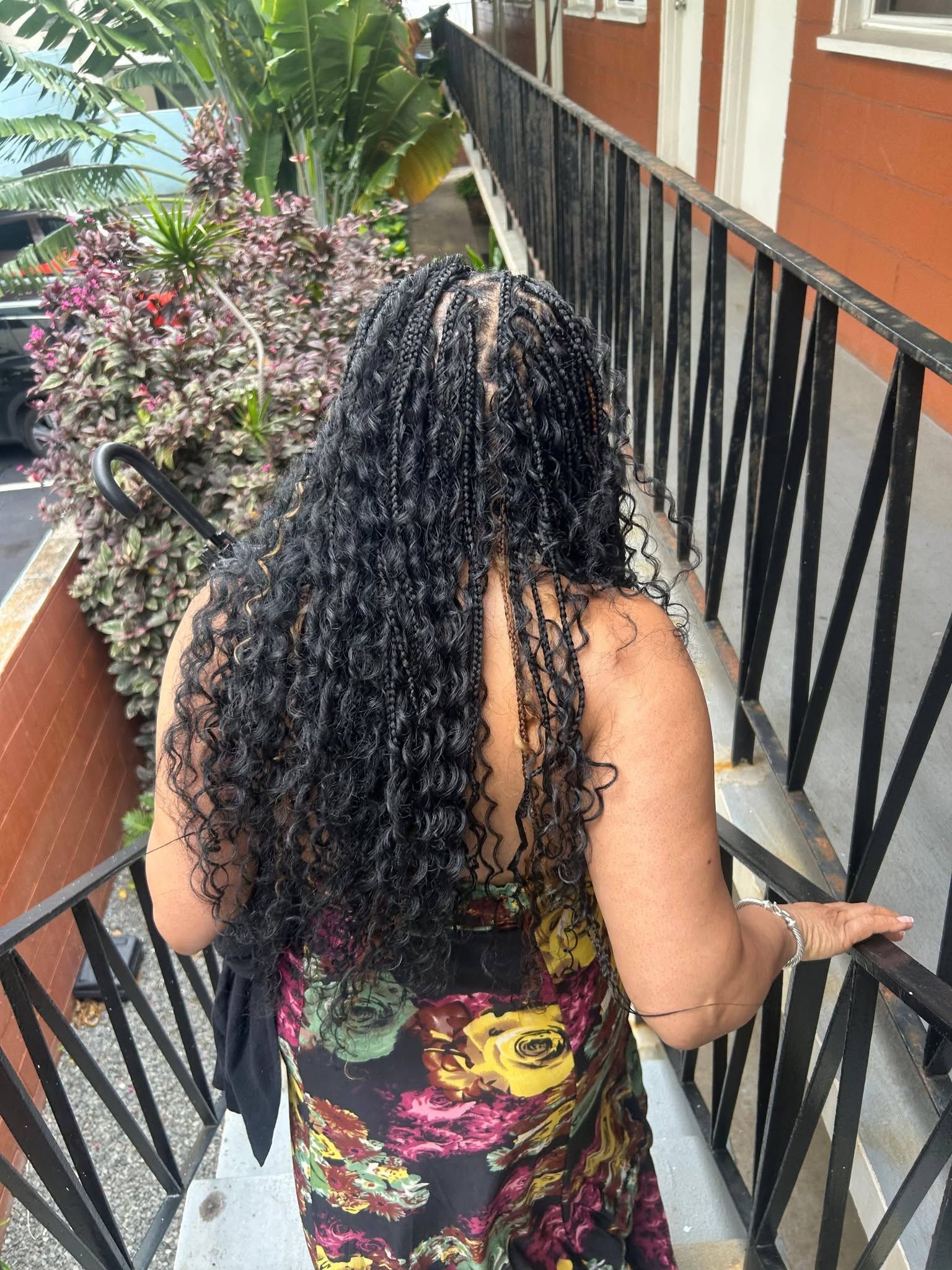 Person with curly hair walking down outdoor stairs beside a black railing and tropical plants