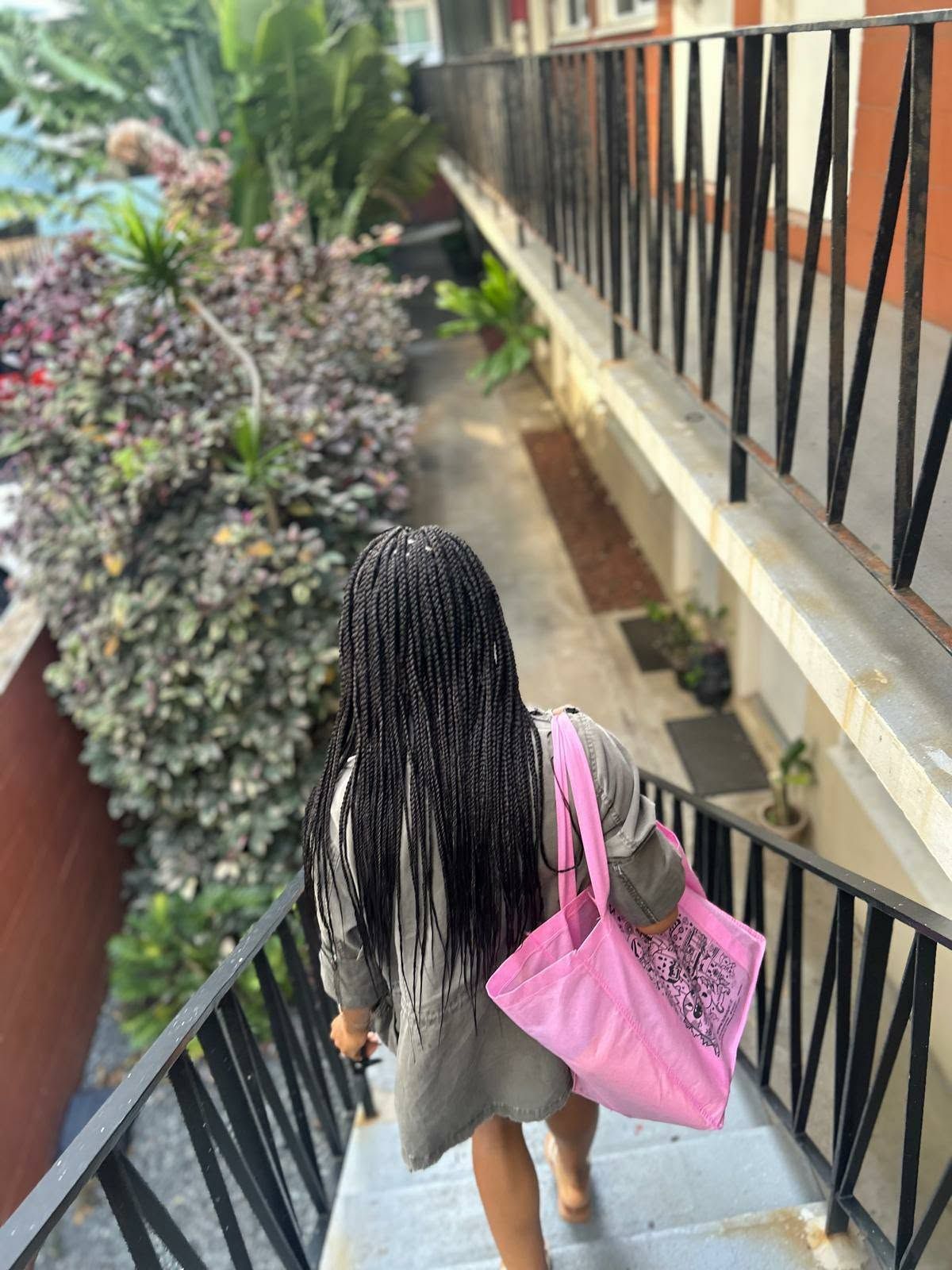 Person with pink tote descends outdoor stairs beside a railing and landscaped greenery.