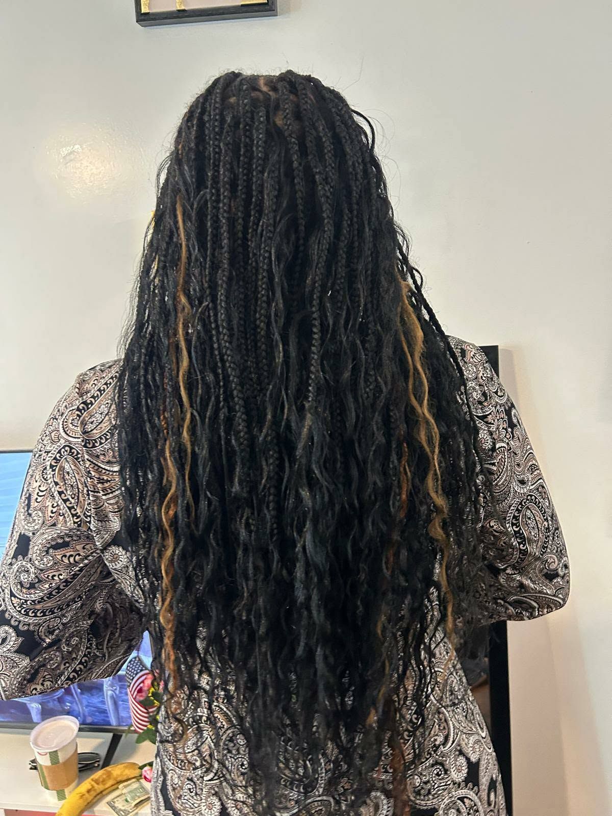 Person with long black braids standing indoors, seen from behind, wearing a patterned sweater.