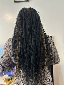 Person with long black braids standing indoors, seen from behind, wearing a patterned sweater.