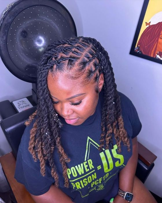 Woman with braided hair looking down in a navy T-shirt, seated near a large speaker.