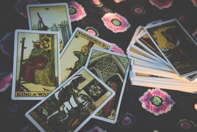 Su un telo scuro e decorato è steso un mazzo di carte dei Tarocchi, tra cui carte ben visibili come il Re di Bastoni e un mazzo impilato.
