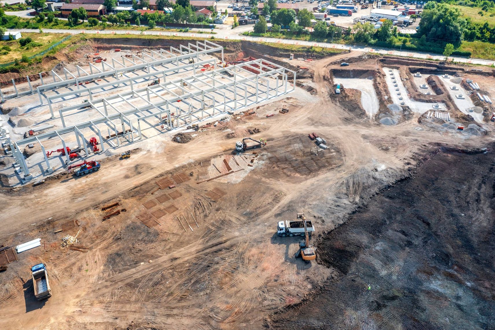 Aerial view of a large construction site with steel-framed buildings, dirt roads, and excavators.