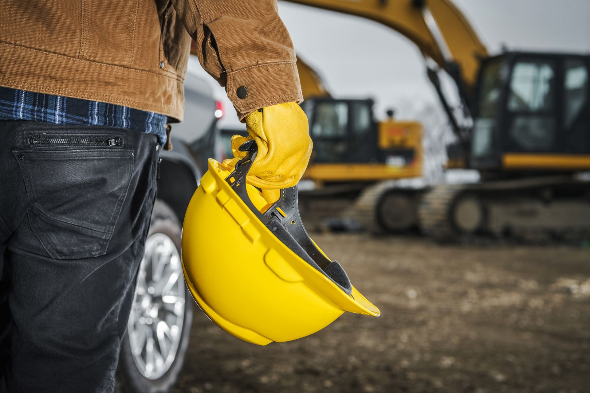 Worker in yellow gloves holding a yellow hard hat at a construction site.