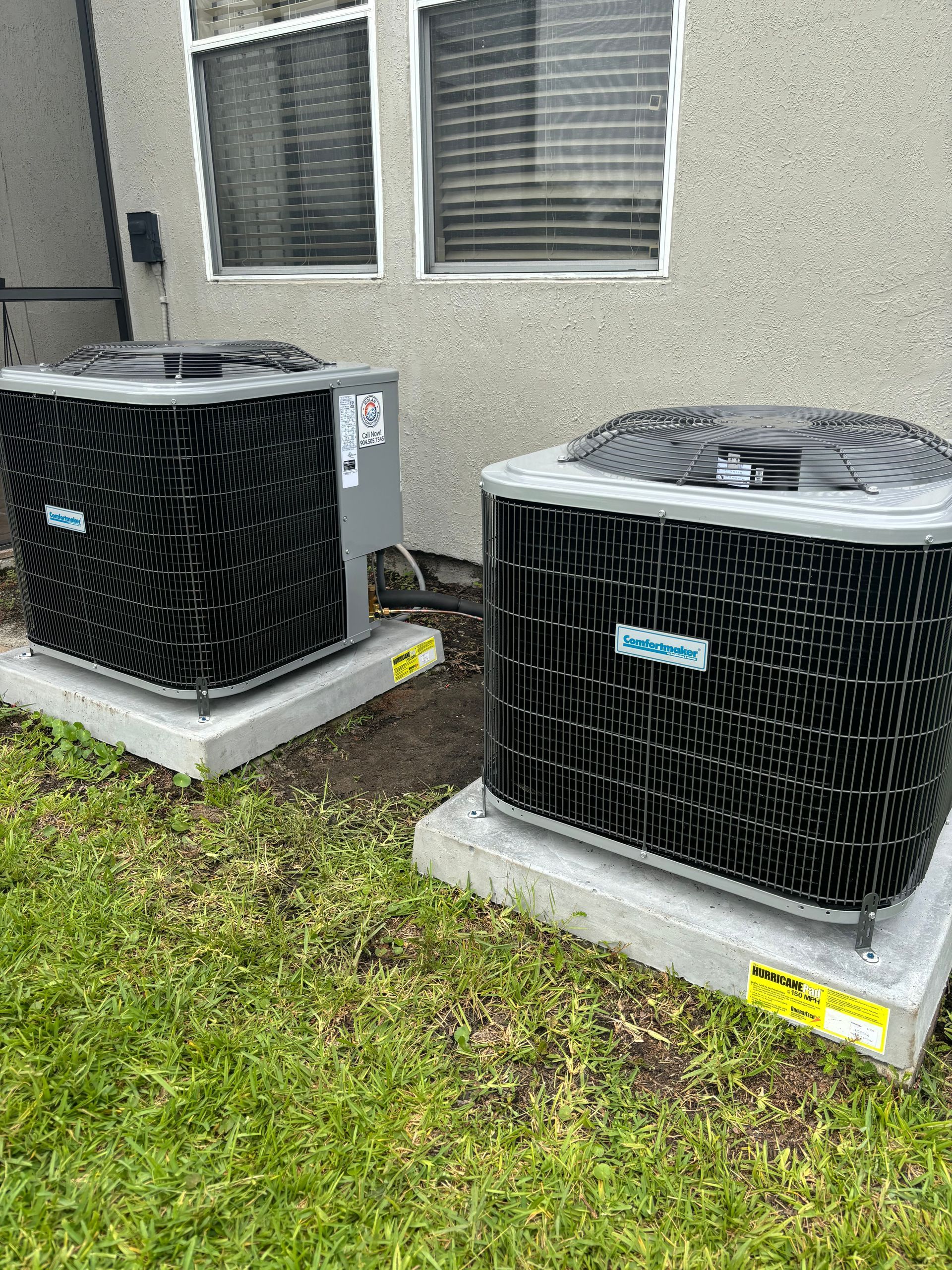 Two air conditioners are sitting next to each other in front of a house.