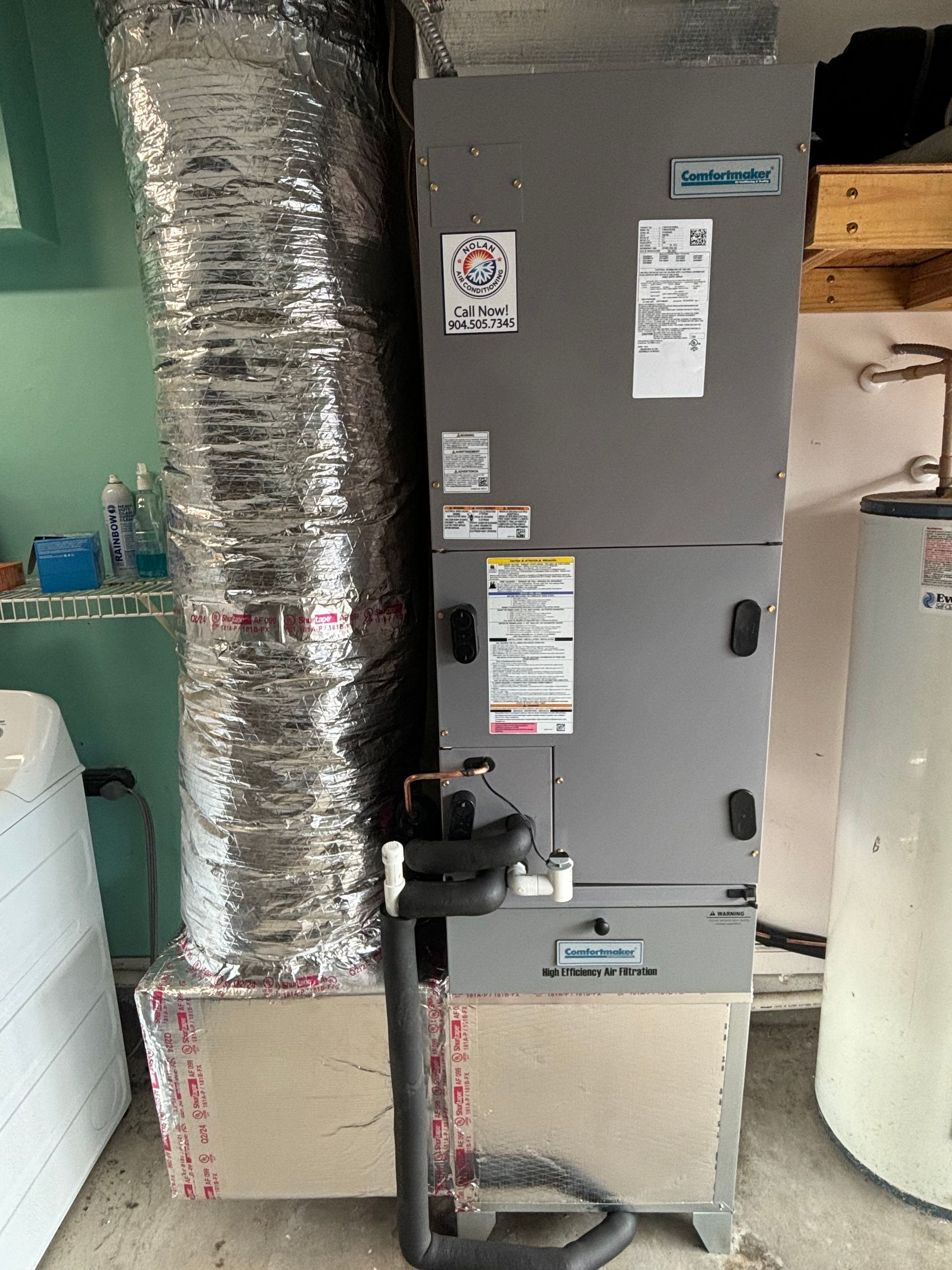 An air conditioner is sitting in a garage next to a water heater.