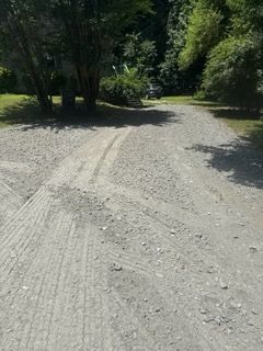 Gravel road curving through a shaded green wooded area in bright sunlight