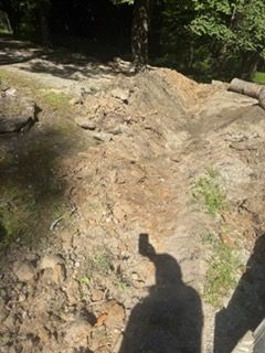 Rough rocky trail in a wooded area, with a person’s shadow in the foreground.