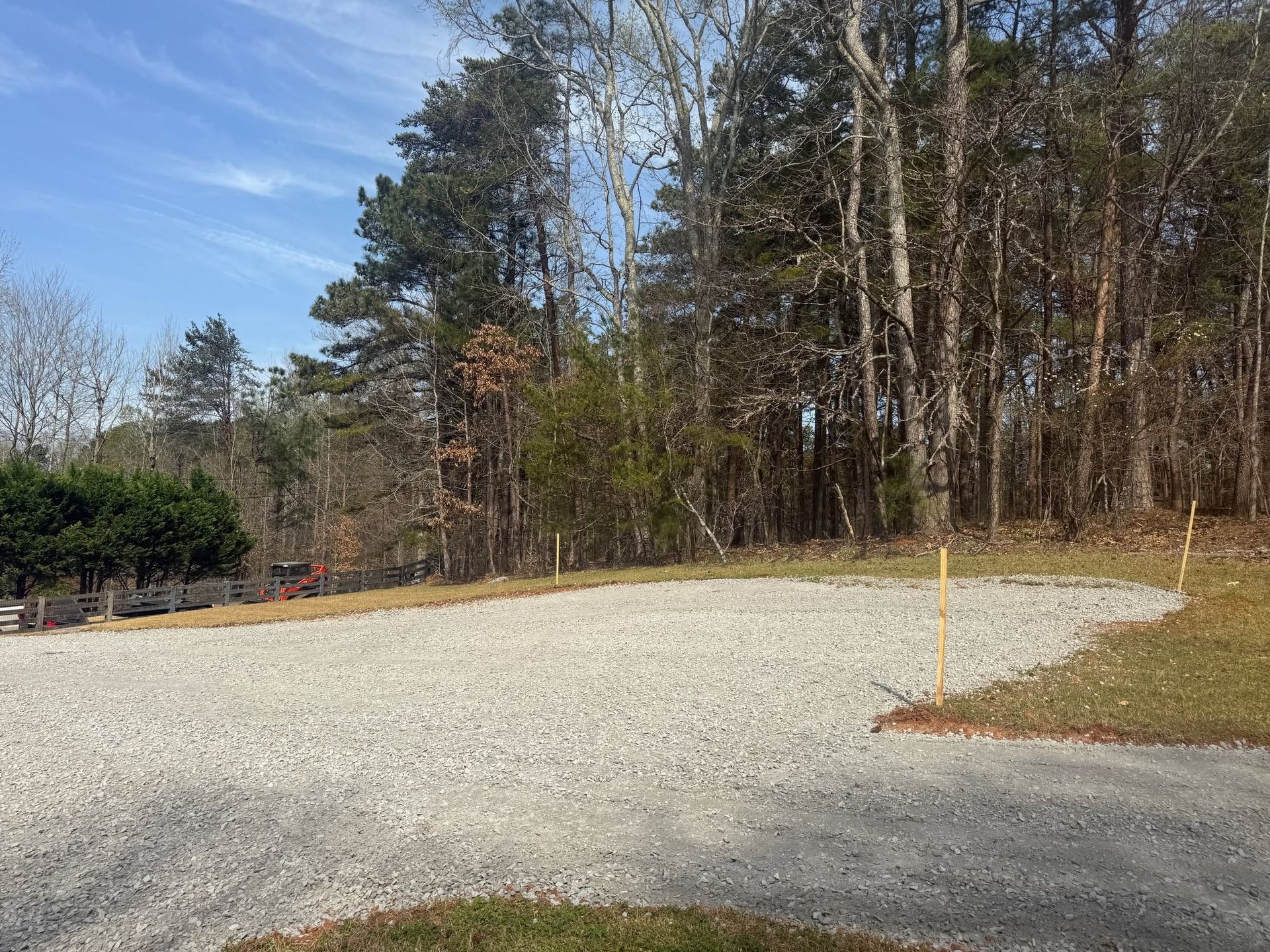 Gravel parking area beside a wooded tree line under a blue sky