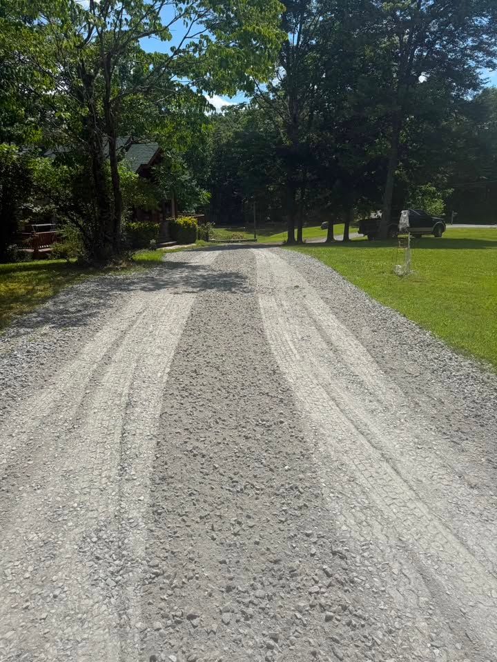 Farm road with a black tractor implement grading muddy dirt track alongside grass.